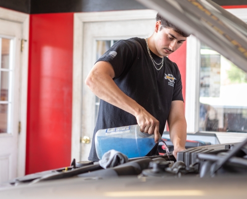 technician adding fluid and lubricants under hood of vehicle.