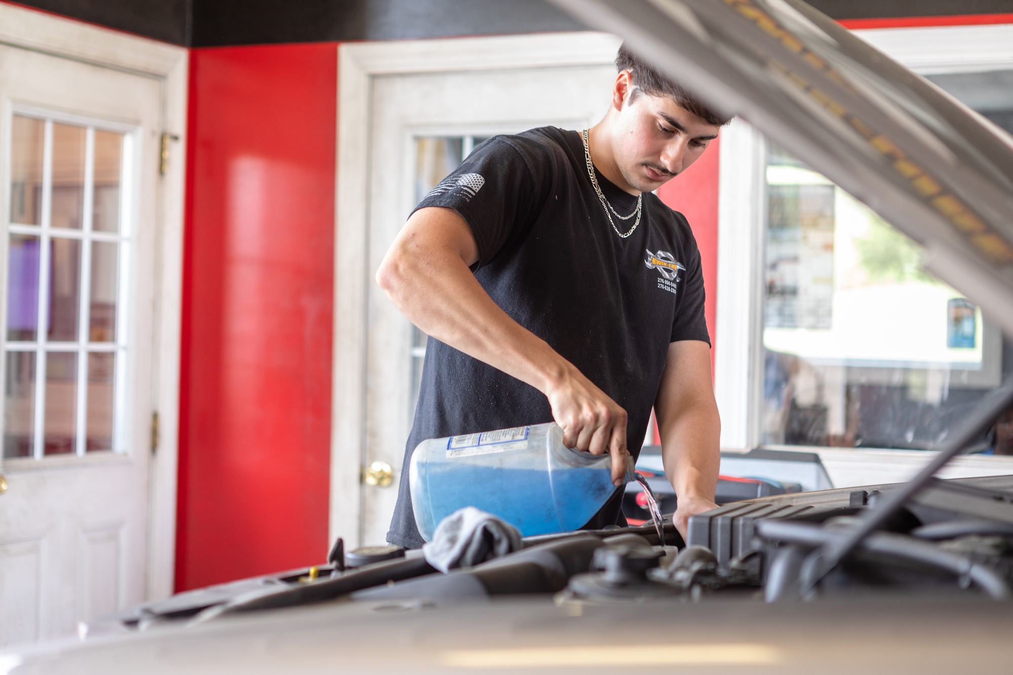 technician adding fluid and lubricants under hood of vehicle.